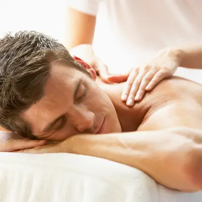 Man relaxing face down while a massage therapist works on his upper back